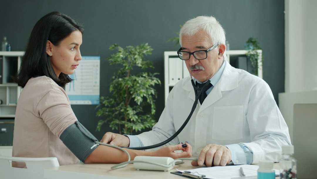 Doctor checks patient's blood pressure with stethoscope and monitor.